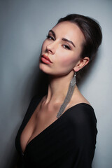Portrait of a beautiful fashionista brunette girl, with long silver earrings, in black with a neckline on a light white background in the studio room
