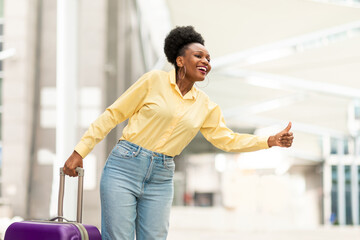 Cheerful Black Female Tourist Catching Taxi With Gesture At Airport