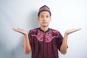 a Muslim wearing a koko shirt and cap with confused gesture isolated on white background.