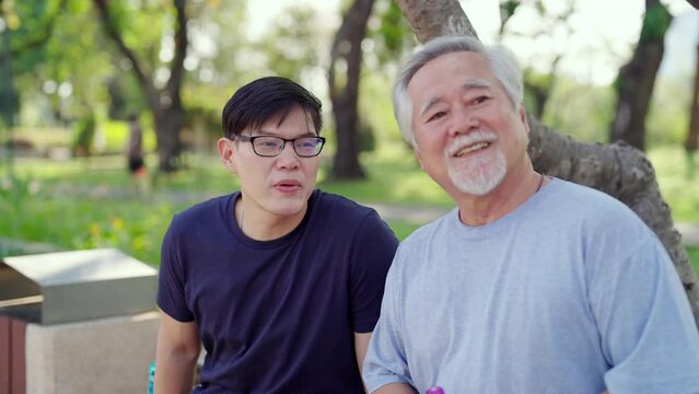 Asian adult son and elderly father looking urban cityscape during jogging exercise together at park. Retired man enjoy outdoor sport workout. Family relationship and older people health care concept.