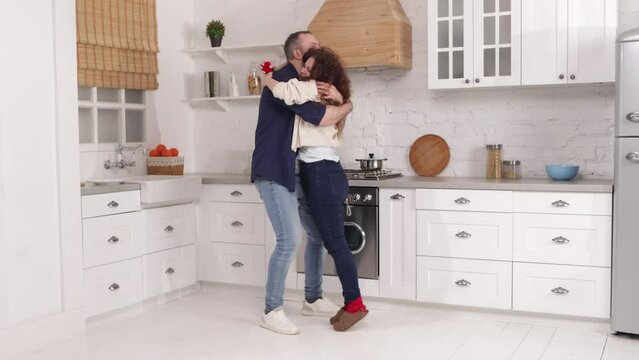 Portrait of caucasian girlfriend proposing her partner in their cozy kitchen. Beautiful heterosexual couple hugging and looking happy after engagement. High quality 4k footage