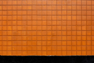 An abstract image of an exterior wall built with orange and black square bricks. 
