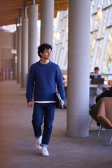 Handsome Hispanic male student, holding laptop and visiting a modern library campus.