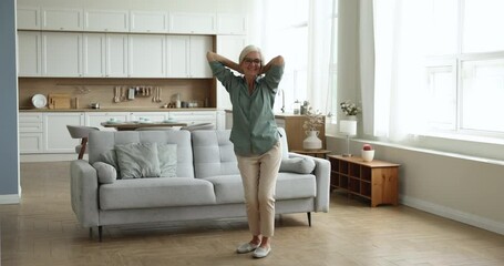 Full-length vivacious older woman dancing, jumping in cozy spacious living room, listen moving to music, looks carefree, feels love to life. Happy elderly female spends weekend or vacation at own home