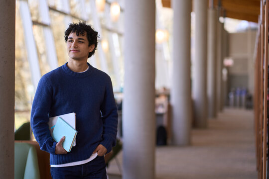 Confident portrait of a thoughtful smiling young Hispanic male student visiting a modern library