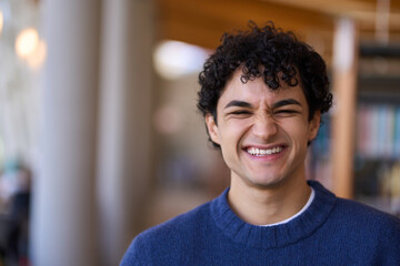 Hispanic male student smiles looking at camera, standing against bookshelves in library or bookstore