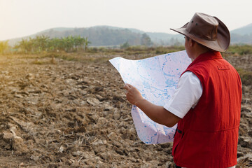 Asian man explorer wears hat, red vest shirt, holds map to explore land boundary. Concept, land planning, exploring property. Geodetic survey area. Treasure  hunting on land. Adventure lifestyle.     