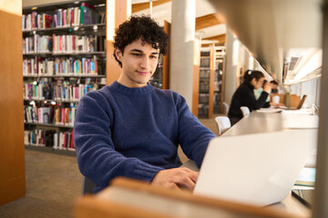 Latin American male student using laptop, making researches on internet in modern innovation library