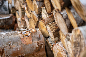 A cord of cut birch wood for firewood piled high under a blue sky with white clouds. The long logs...