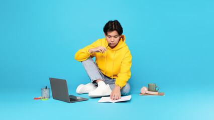 Asian Teen Boy Using Laptop Sitting On Floor, Blue Background