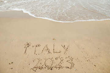 Italy 2023 lettering on the beach with wave and clear blue sea. 
