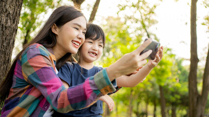 Happy Asian mother using mobile phone selfie or Video call with her son outdoors - Family and love concept. Mother’s day celebration.