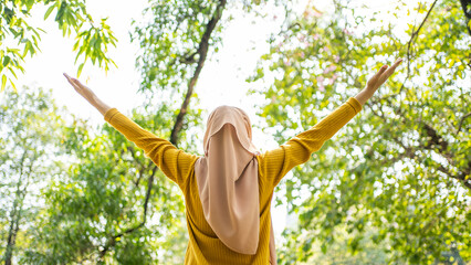 Young Muslim woman arms raised stretching and enjoying the fresh air in green forest. Enjoying the...