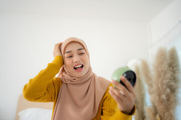 Terrified young Muslim woman holding alarm clock in bed at home, grabbing her head, oversleeping to work. Shocked millennial lady being late, having difficulty getting up in mornings.