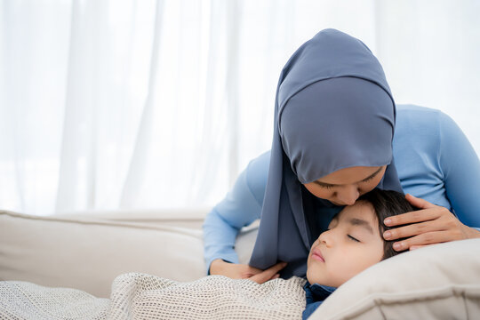 Closeup photo of caring Asian mother holding head on sick son forehead.