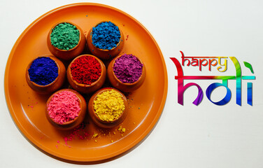 Various Holi paints in pots on a tray with a colorful inscription Happy Holi. Colorful background for the national Indian holiday Happy Holi. White background, top view.