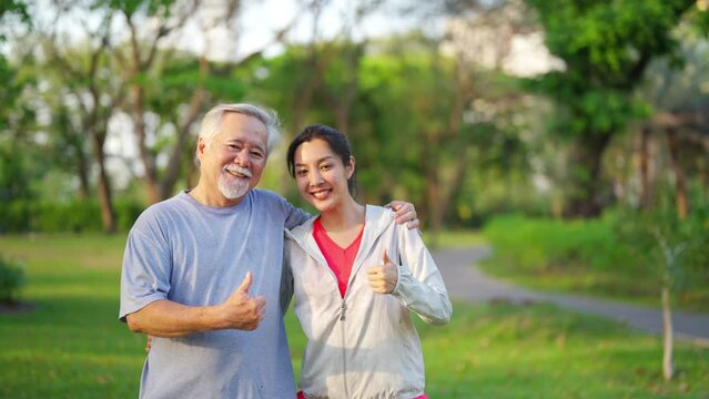 4K Happy Asian daughter and elderly father in sportswear jogging exercise together at park. Retired man enjoy outdoor lifestyle sport workout. Family relationship and senior people health care concept