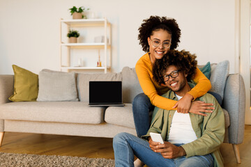 Happy Black Couple Hugging And Using Smartphone At Home