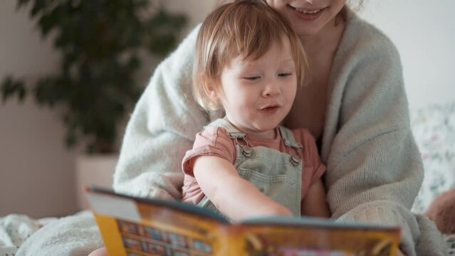 Caring single parent young mother babysitter hug happy cute little preschool child girl kid daughter hold learn read book fairy tale story bonding enjoying family lifestyle hobby at home sit on couch