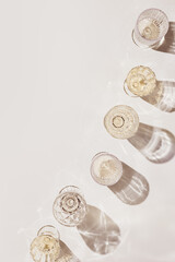 Summer party drinks flat lay, wine glasses with white sparkling wine and sunshine shadow on light table. Minimal pattern with beautiful wine glasses, above view still life, beige golden color