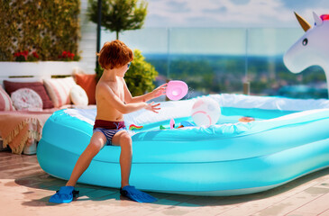 excited kid having fun sitting on inflatable pool on summer patio - 577877945
