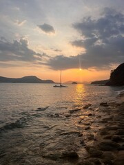 Sunset on the sea of Thailand beach. The sky in the rays of the sun. The sun is setting Sandy sand on the beach. Stones on the beach. lunar path from the sun to the sea. Beautiful mountains in the sea