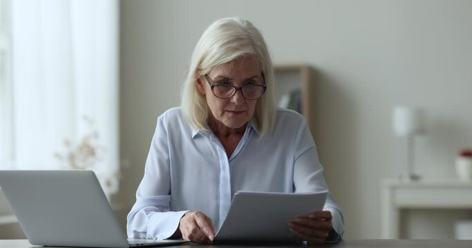 Mature business woman sits at workplace desk holding documents reading bad news in letter feels angry, mad, throw papers, get dismissal notice, bank debt, eviction notification, mortgage denial, fine