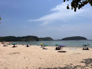 Thai beach Nai Harn. Yellow sand and the sea Sunbathing people on the beach under an umbrella.