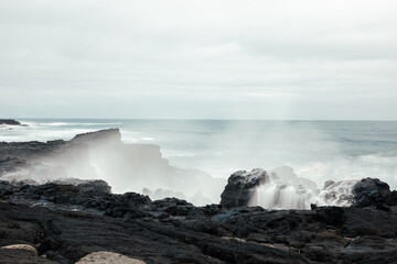 Long exposure of wave hitting black rocks