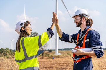 Caucasian man and woman engineers in uniform discuss with shaking hands stand near wind turbines...