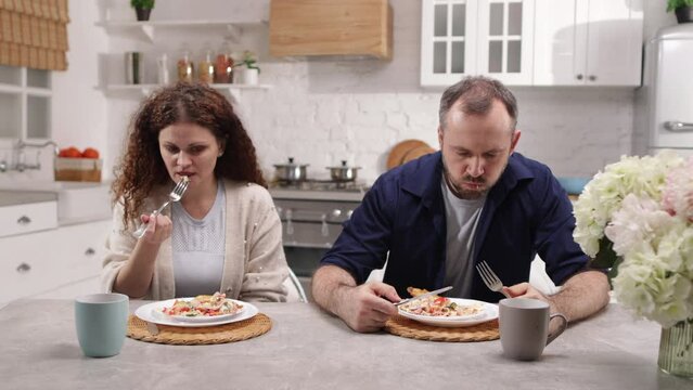 Portrait of dissatisfied man eating breakfast with his beautiful, scared wife. Annoyed man looking angry and abusive while sitting by his girlfriend. High quality 4k footage