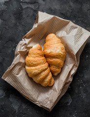 Fresh crispy croissants on a paper bag on a dark background, top view