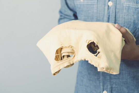Used wrong type of washing powder concept. Man holding yellow torn and old T-Shirt. Studio shot on grey wall.