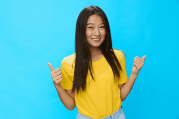 Asian woman points to a loose background in a yellow T-shirt and blue jeans on a blue background