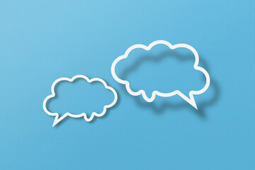 White paper cut out speech bubble shapes set on light blue paper background.