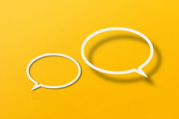 White paper cut out speech bubble shape set on yellow paper background.