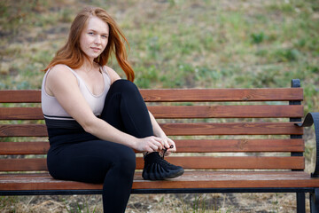 a girl sits on a bench in sportswear and ties a shoelace