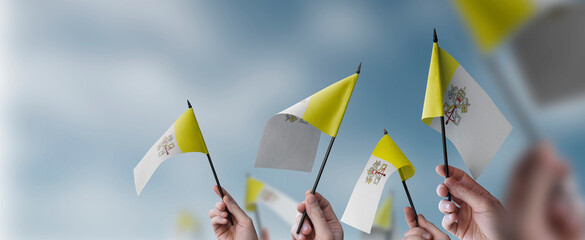 A group of people holding small flags of the Vatican in their hands