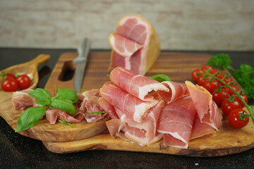 Traditional Italian smoked ham close-up composition with basil, tomato and knife