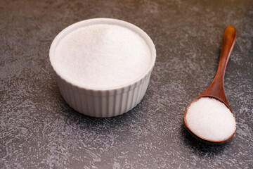 Erythritol, organic sweetener, produced by fermentation from corn, called dextrose in ceramic bowl, wooden spoon on granite background, table. Sugar substitute. Horizontal plane