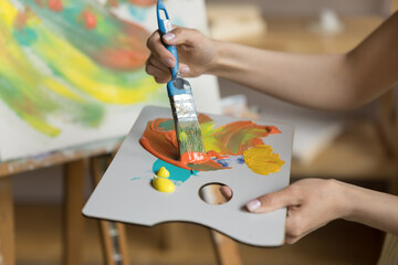 Hand of artist blending paints for drawing, mixing colors on palette, using paintbrush, working on...