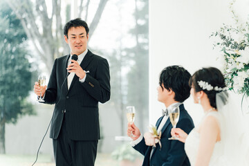 結婚式で乾杯の挨拶をする男性と新郎新婦
