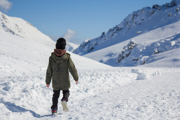 A boy walks alone through a snowy valley. Mountains in the snow.
