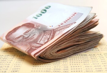 Saving account bank book/pass book with updated entries of deposit and withdrawal, and Thai cash money bank notes on it, in concept of money saving or Thai economy