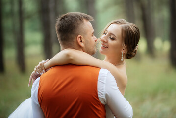 Fototapeta premium young couple bride in a white short dress and groom in a gray suit in a pine forest
