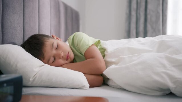 Cute 5 years old boy sweetly sleeping in comfy bed. Face close-up of sleeping child. Dolly shot sleeping kid at early morning. Relax and rest concept for child heath. 4k footage sleeping child in bed