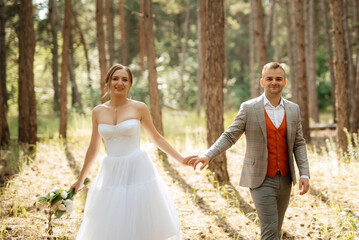 young couple bride in a white short dress and groom in a gray suit in a pine forest