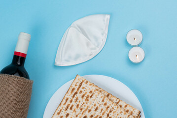 Matzah, Shabbat candles, wine and Jewish kippah on blue background. Pesah Passover holiday celebration dinner concept.