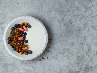 Nut granola bowl with yogurt, blueberry and strawberry. Healthy breakfast with oat crunchy muesli. Grey background. Top view. Copy space
