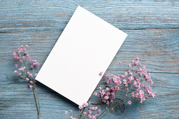 Card mockup, white blank wedding invitation with floral decor on bue wooden background. Greeting...
